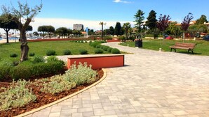 A paved walkway with benches, a landscaped area with shrubs, and a clear sky. - Comfortable apartment in Valizza-Umag, surrounded by greenery, air-conditioned (Valica)