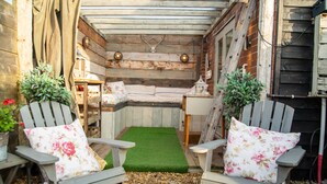 A cozy outdoor seating area with Adirondack chairs, a small bench, and a green turf rug. - The Cowshed 5* Barns (Wrenbury, Nr Nantwich)