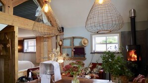 A cozy room with a wooden ceiling, a fireplace, and a dining area with a table set for two. - The Cowshed 5* Barns (Wrenbury, Nr Nantwich)