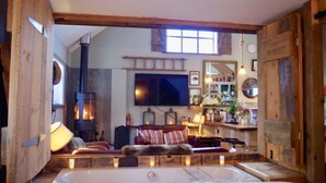 A cozy room with a fireplace, a large flat-screen TV, and a wooden bench. - The Cowshed 5* Barns (Wrenbury, Nr Nantwich)