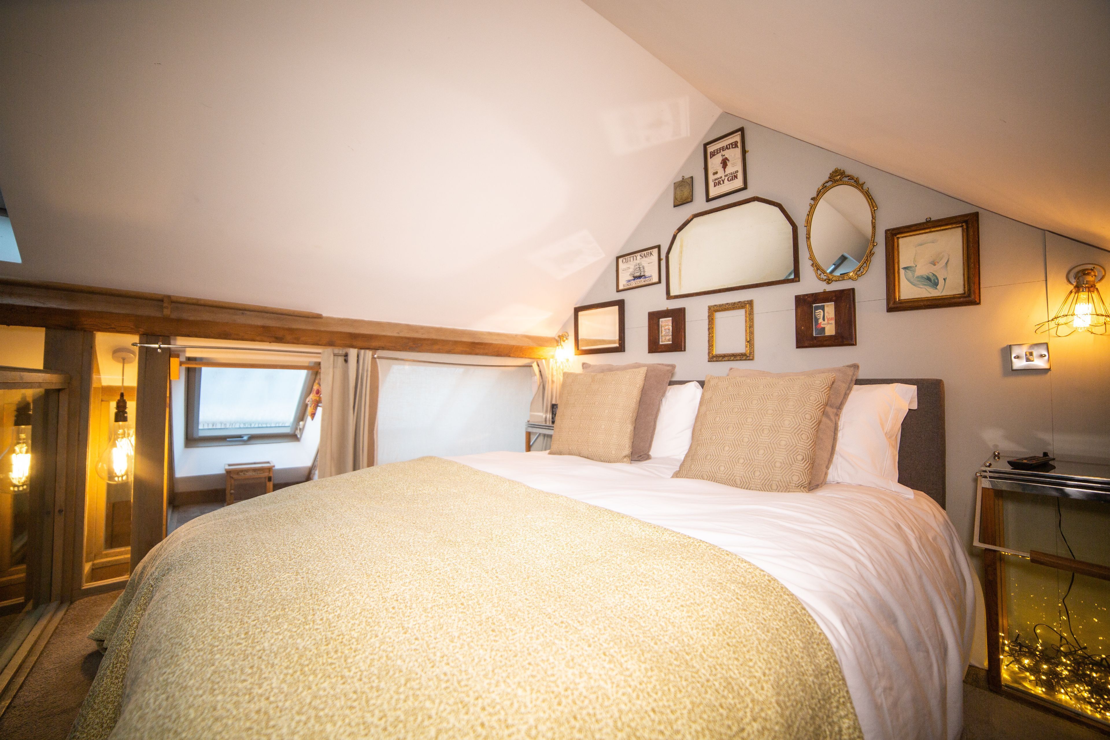 A hotel room with a large bed, a bedside table, a mirror, and wall-mounted picture frames.