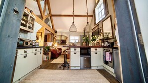 A kitchen with white cabinets, a wooden ceiling, hanging light fixtures, and a built-in oven. - The Cowshed 5* Barns (Wrenbury, Nr Nantwich)