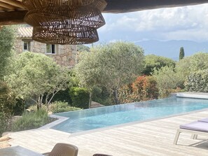 Ein Poolbereich mit Holzterrasse, Liegestühlen und einem dahinterliegenden Steinhaus.
