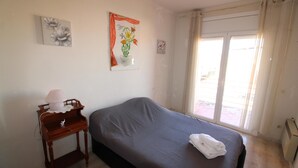 A bedroom with a bed, a bedside table with a lamp, a window with curtains, and a wall with a framed picture. - Three bedroom apartment with sea views (Empuriabrava)