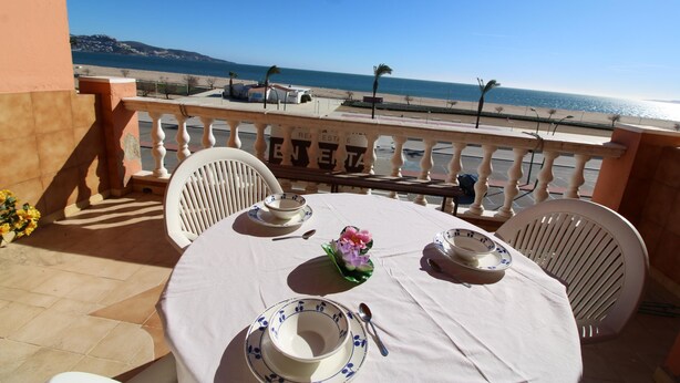 A balcony table set with white tablecloth and blue plates, overlooking a beach and sea. - Three bedroom apartment with sea views (Empuriabrava)