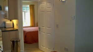 Une chambre d’hôtel compacte, dotée d’une kitchenette, d’un lit recouvert d’une couverture rouge et d’une porte donnant sur une autre pièce.