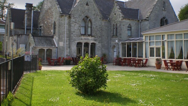 Un bâtiment historique en pierre, doté d’une cour, de chaises rouges et d’une véranda.
