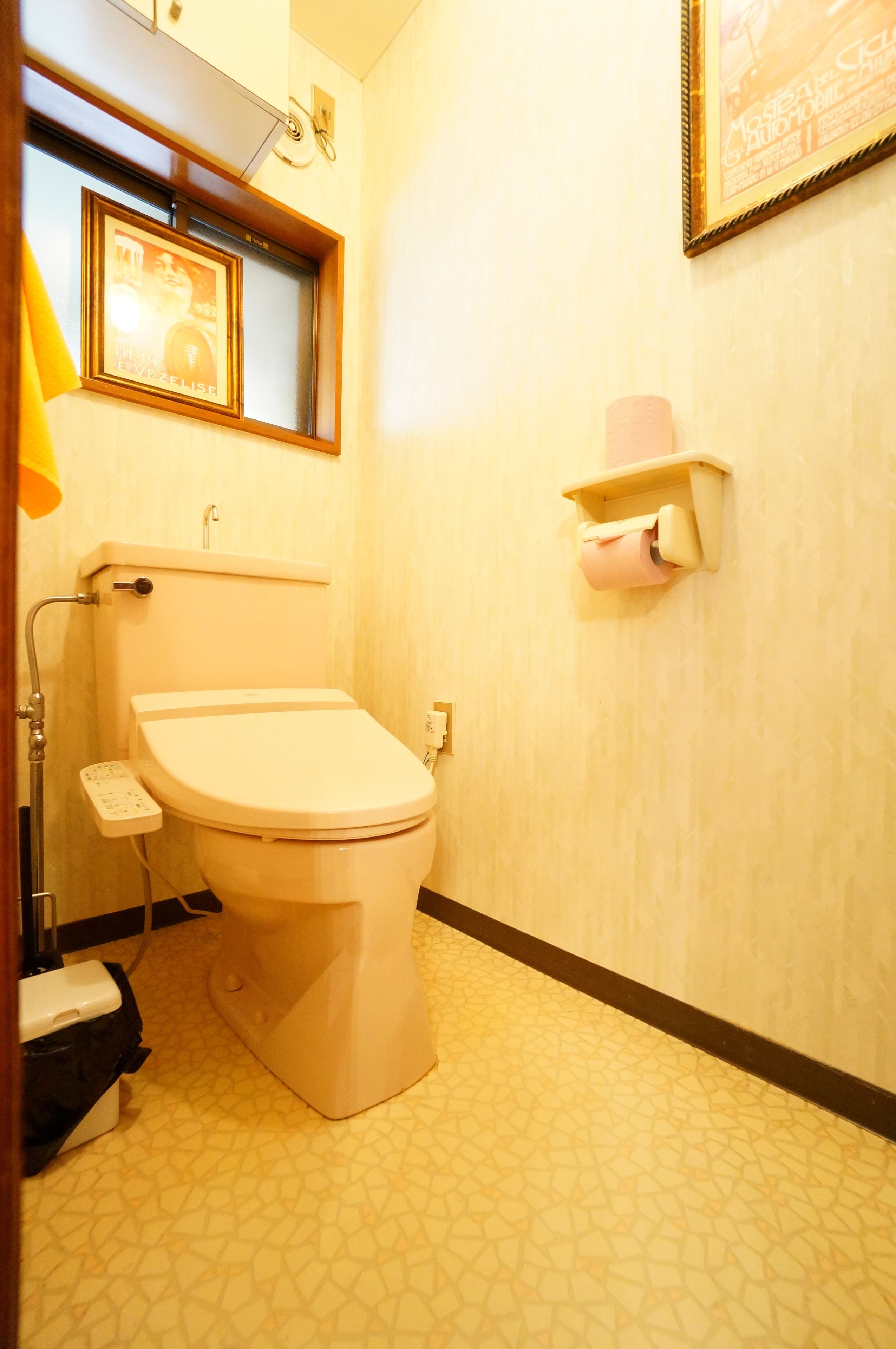 A bathroom with a toilet, a hand dryer, a towel rack, and a framed picture on the wall.