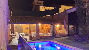 Una piscina con diseño geométrico, rodeada por una valla y un patio con mobiliario exterior.
