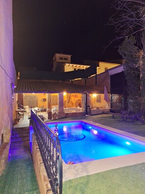 Une piscine au design géométrique, entourée d’une clôture et agrémentée d’un patio avec des meubles d’extérieur.
