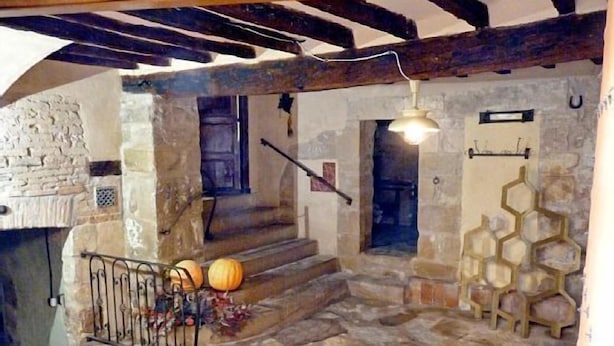 Interior con piso de piedra, una escalera, una puerta de madera y una lámpara fijada a la pared.