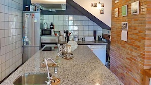 Una cocina moderna con encimera de granito, electrodomésticos de acero inoxidable y una pared de ladrillo decorativa.
