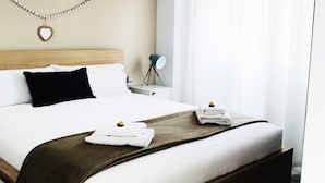A neatly made bed with white linens and a brown throw blanket, a wooden headboard, a wall-mounted heart-shaped decoration, and a hanging woven light fixture. - Cozy and comfortable, best location! Ideal for families. (Costa Adeje)
