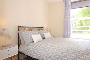 A neatly made bed with a patterned bedspread and pillows, a bedside table with a lamp, and a window with curtains.