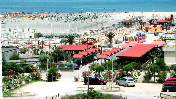 A beach resort with multiple red-roofed buildings, a sandy beach, and a view of the sea. - HOLIDAY RESIDENCE: sea and shopping within reach. (Lido degli Estensi)