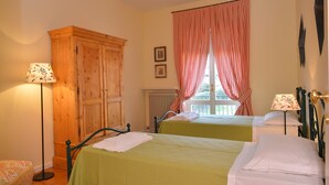 A room with two beds, a wooden wardrobe, and a window with red curtains.