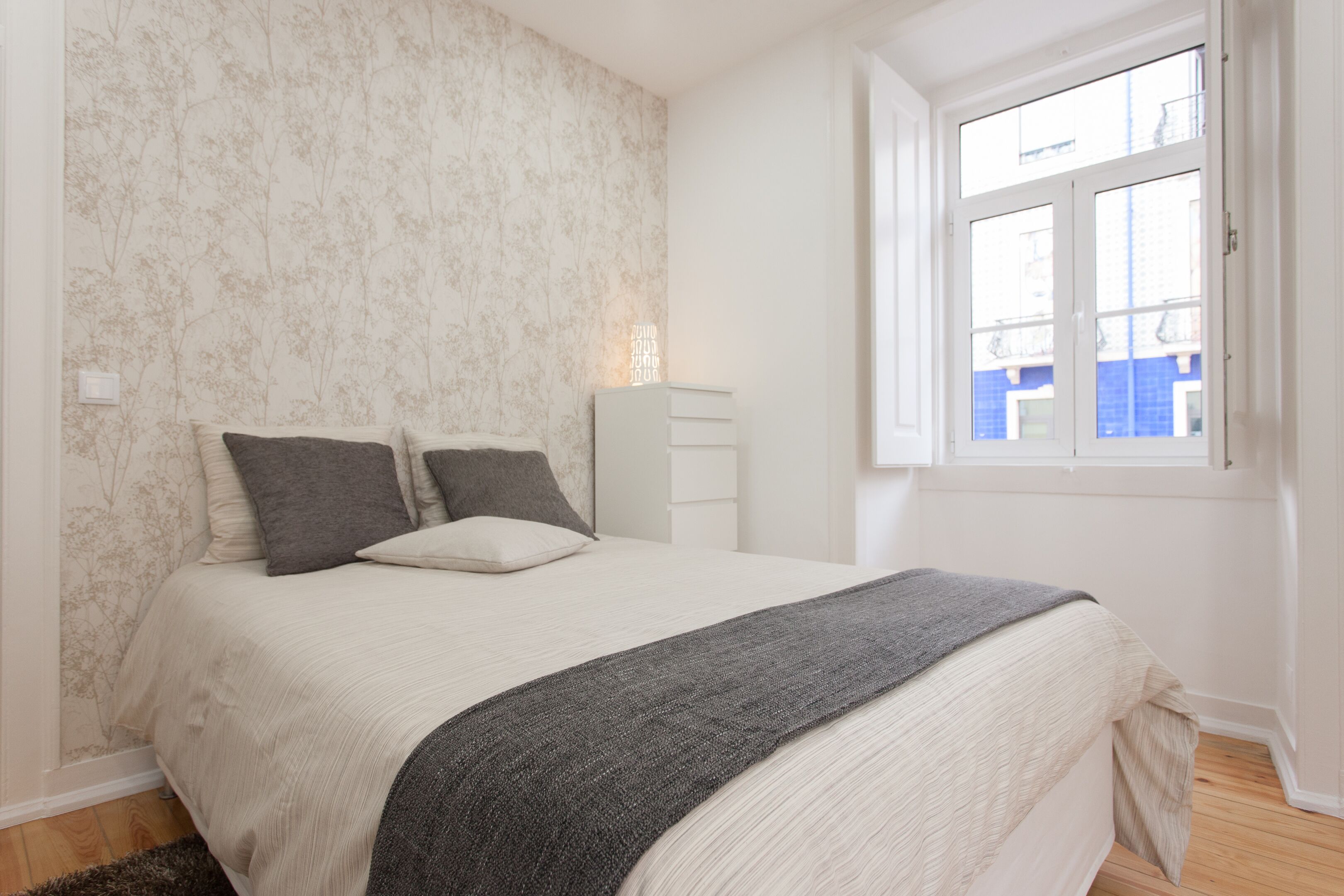 Une chambre à coucher avec un lit, une fenêtre et un mur orné d’un motif floral.