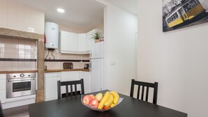 Una cocina moderna con armarios blancos, lavavajillas y estufa. Hay una mesa de comedor con un frutero en el centro.