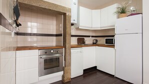 Una cocina con armarios blancos, horno de acero inoxidable, lavavajillas, microondas y refrigerador.