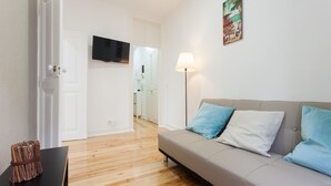 Una sala moderna con un sofá, un televisor de pantalla plana montado en la pared y una lámpara.