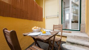 Una mesa de madera con alimentos para el desayuno, una silla y vista a un edificio a través de un vidrio.