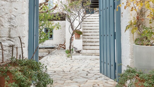Un chemin de pierres mène à travers un bâtiment aux murs blancs, doté d’une porte et d’une arche bleue.