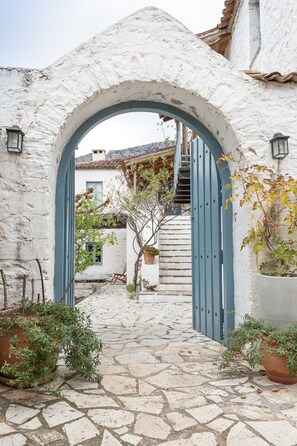 A stone pathway leading through a white-walled building with a blue door and archway.