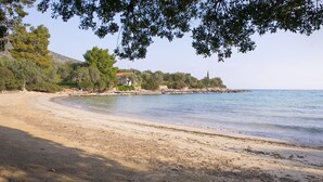 Une plage de sable fin, avec une eau claire, des arbres et un bâtiment visible au loin.