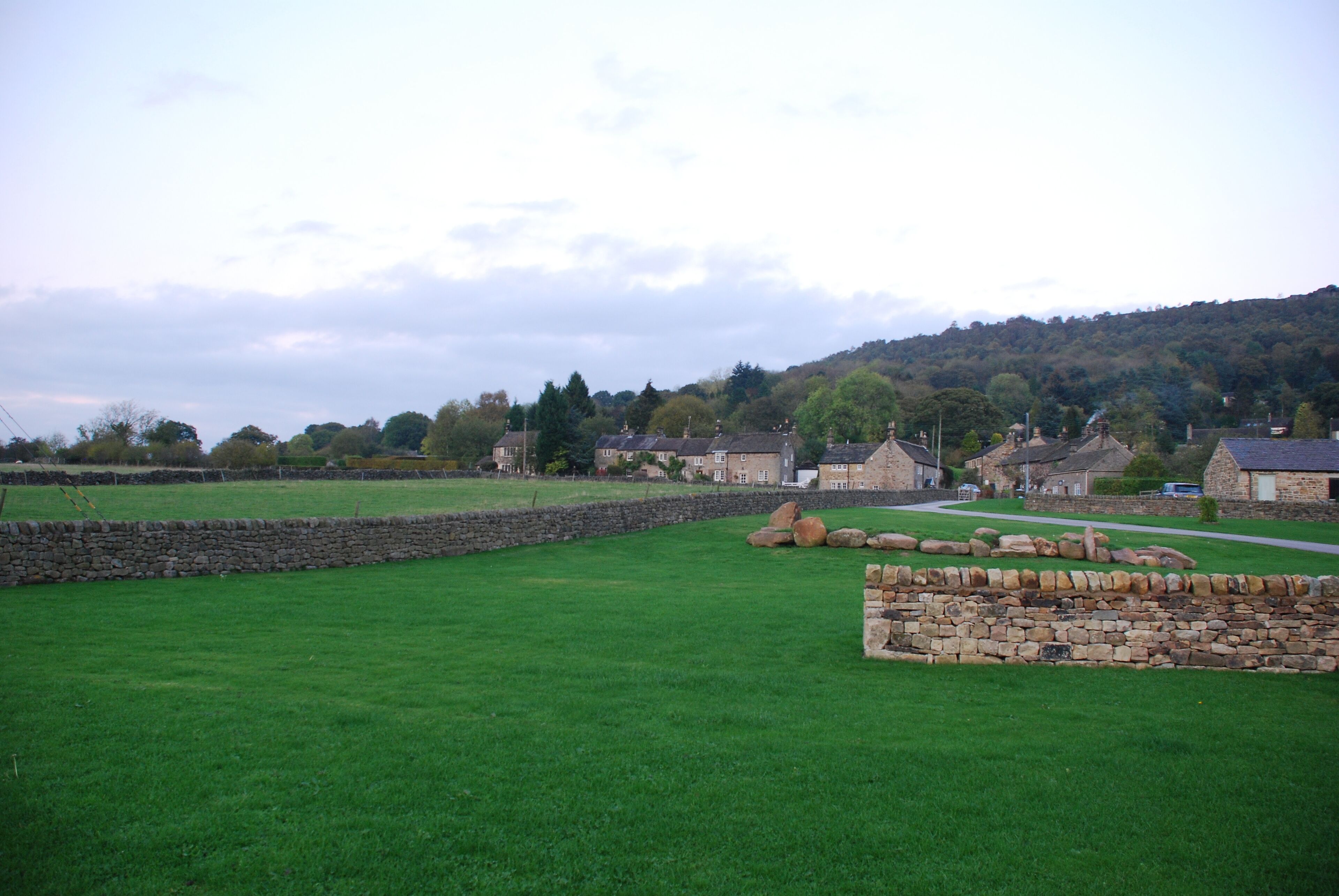 Un paysage rural avec des murs de pierre, un champ d’herbe et des maisons en arrière-plan.