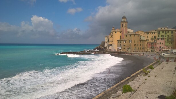 Une ville côtière dotée d’un clocher d’église imposant, d’une plage aux vagues déferlantes et de bâtiments aux couleurs vives.