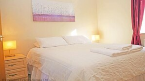 Habitación de hotel con una cama grande, dos mesitas de noche con lámparas, un cuadro en la pared y una ventana con cortinas.