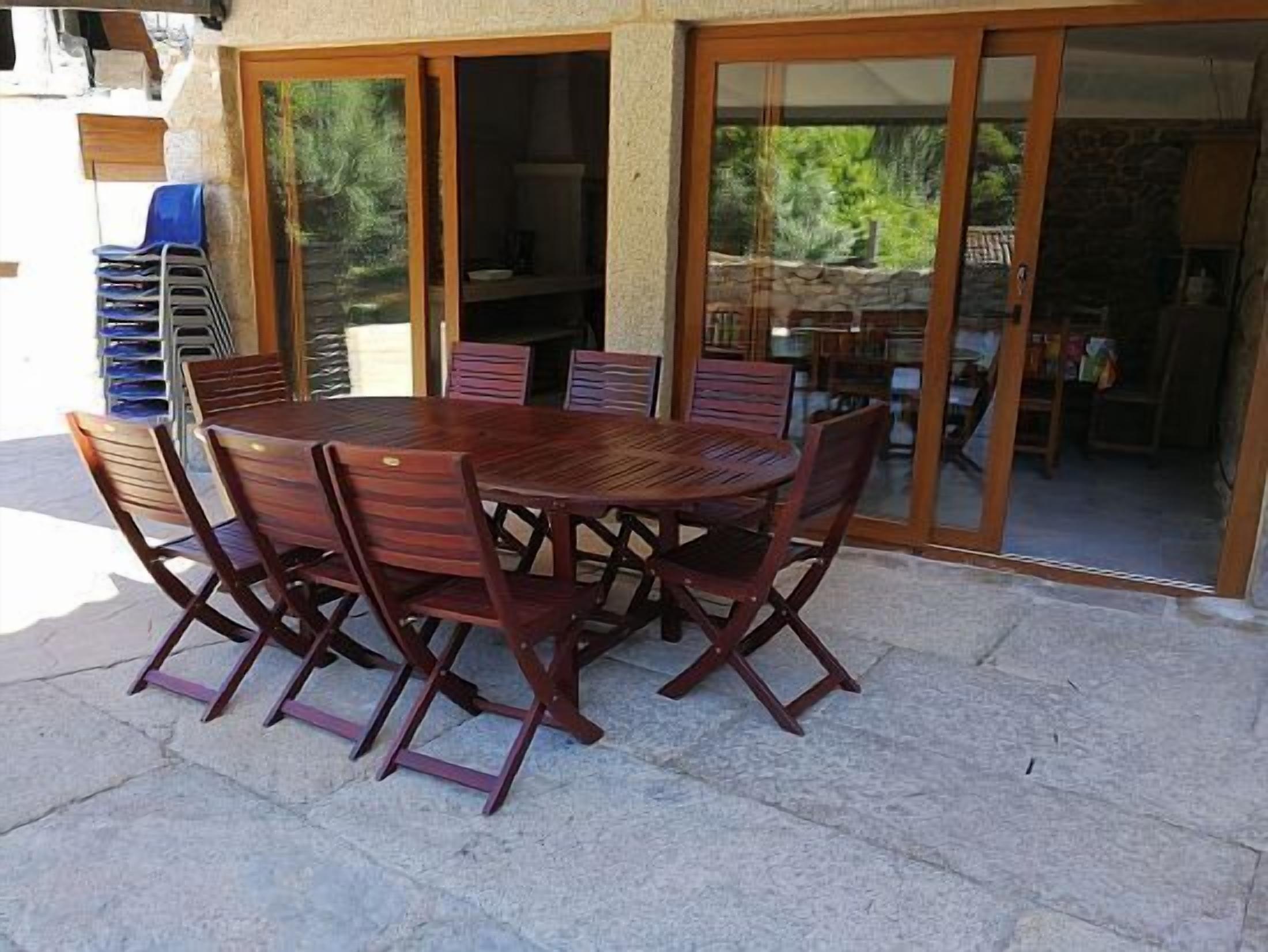 Eine Außenpatio mit Holztisch und -stühlen, umgeben von Steinmauern und einer Glastür, die in einen Garten führt.