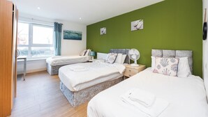 Ett hotellrum med två sängar, ett skrivbord, ett fönster med gardiner och konstverk på väggarna.
