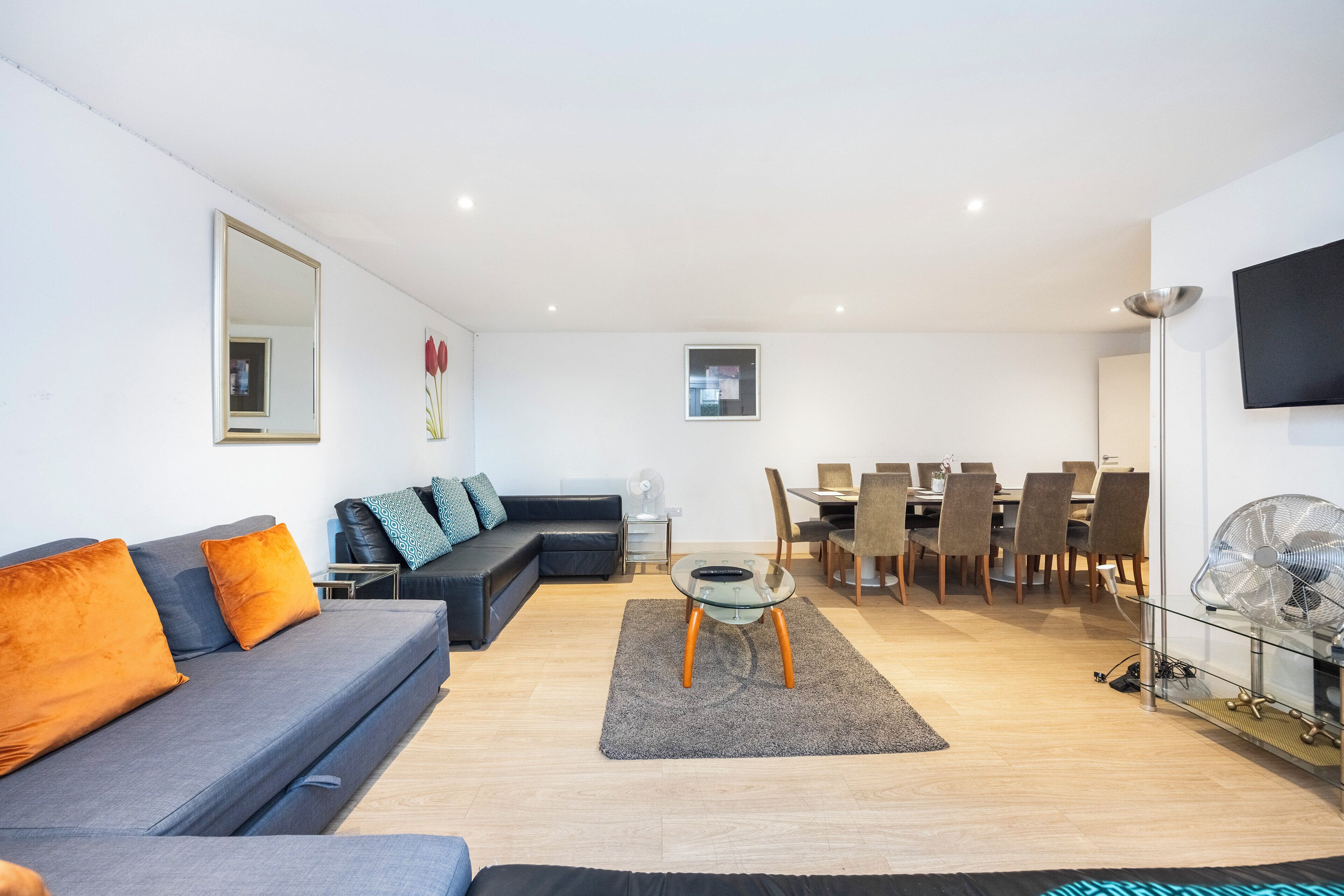 A modern living room with a grey sofa, a glass coffee table, and a dining area with wooden chairs and a table.