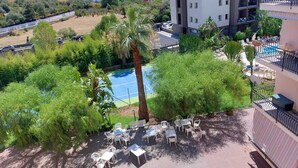 Een hotel met een zwembad, omringd door groen, terrasmeubilair en uitzicht op het omliggende landschap.