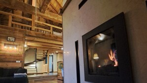 Una habitación acogedora con chimenea, vigas de madera, un sofá y un cesto de basura.