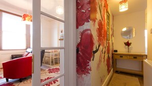 Un corridoio con un murale floreale, una sedia rossa, un tavolo consolle in legno e uno specchio a parete.