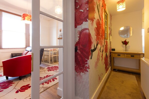 A hallway with a floral mural, a red chair, a wooden console table, and a mirror on the wall.