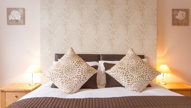 Un letto rifatto con cuscini decorati, una testiera e lampade sui comodini.