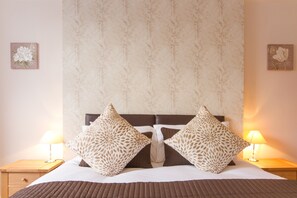 A neatly made bed with patterned pillows, a headboard, and bedside lamps.