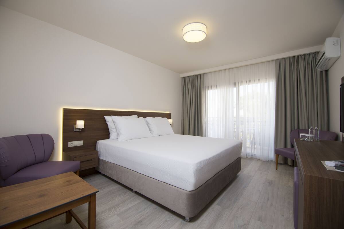 A hotel room with a bed, a desk, a chair, a sofa, and a bedside table.