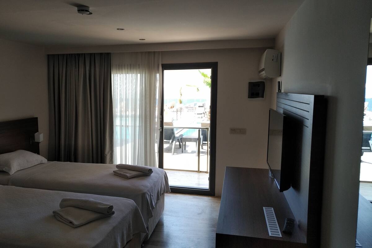 A hotel room with two beds, a TV, a sliding glass door to the outside, and a painting on the wall.