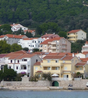 A coastal residential area with multi-story buildings, a stone wall, and a green gate.