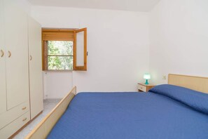 Ein Schlafzimmer mit einem Einzelbett, einem Nachttisch mit Lampe, einem Kleiderschrank und einem Fenster mit Blick ins Grüne.