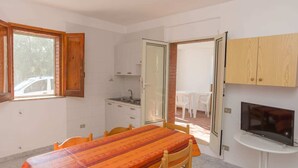 Habitación pequeña con mesa de comedor, sillas, una kitchenette y televisión, además de una puerta corredera que da a un espacio exterior.