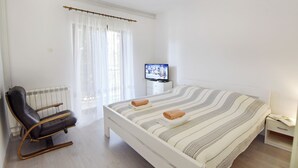 Ein Schlafzimmer mit einem Bett, einem Fernseher, einem Sessel und einem Fenster mit Vorhängen.