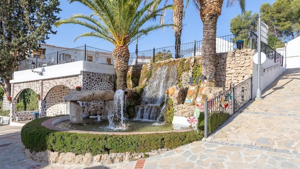 Una fuente de piedra con varios chorros de agua, rodeada por un muro de piedra y palmeras.