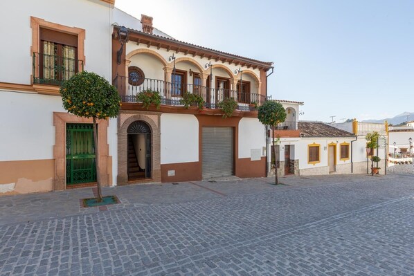 Un bâtiment traditionnel avec un toit en tuiles, un balcon orné de plantes et une rue pavée.