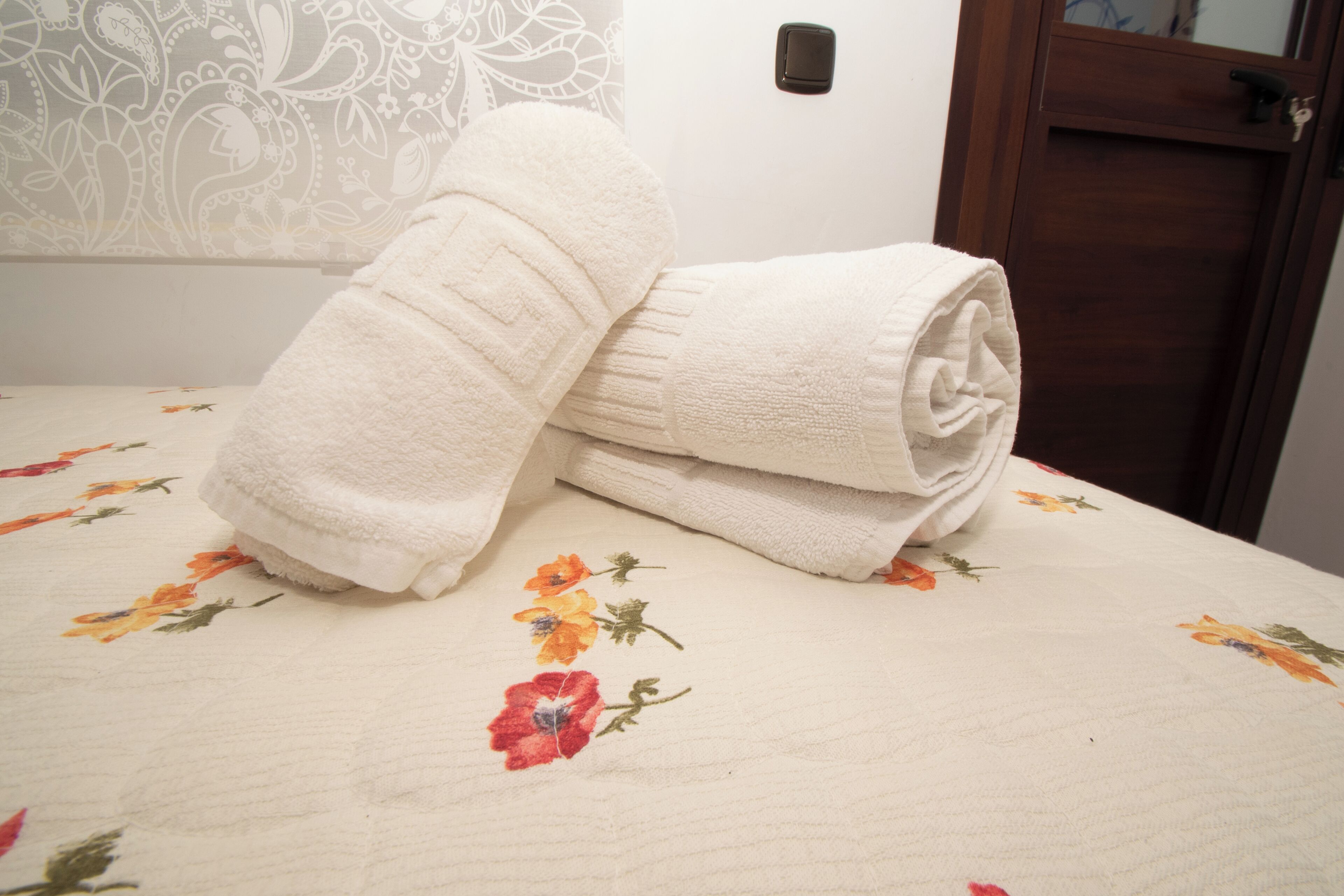 A neatly folded white towel on a floral-patterned bedspread.
