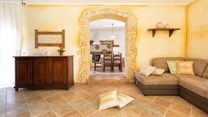 Un salon avec une arche en pierre, un canapé, un meuble et, au fond, un coin repas.